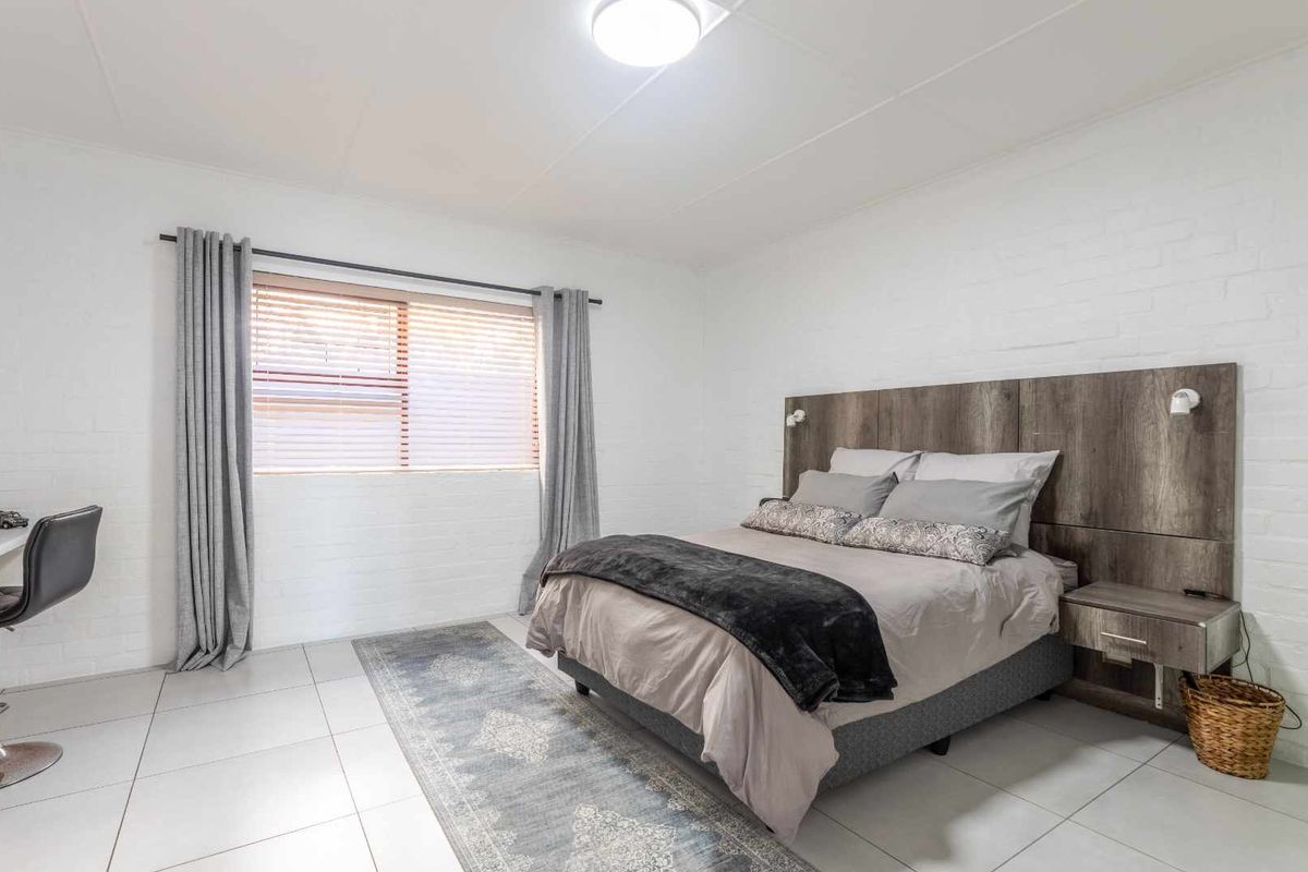 A well-maintained bedroom featuring tiled flooring, painted brick walls, and a modern built-in headboard with integrated lighting.