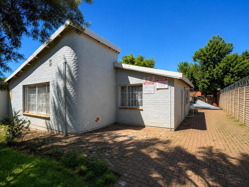 Rear exterior view of the property featuring brick paving, security fencing with razor wire, and visible wear to the exterior wall finish.