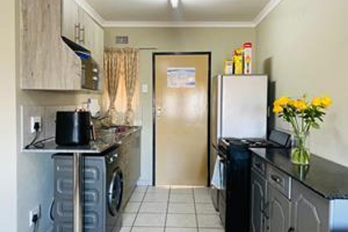 A functional kitchen featuring built-in cabinetry, granite countertops, tiled flooring, and space for a washing machine and freestanding stove.