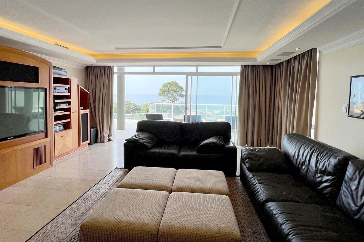 Spacious living room featuring built-in wooden cabinetry, recessed ceiling lighting, and large sliding glass doors opening to a scenic balcony with ocean views.