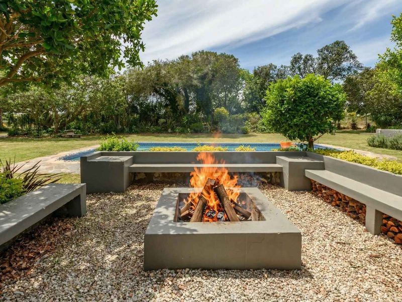Outdoor entertainment area featuring a swimming pool and a central built-in concrete fire pit with integrated bench seating, set within a landscaped garden.
