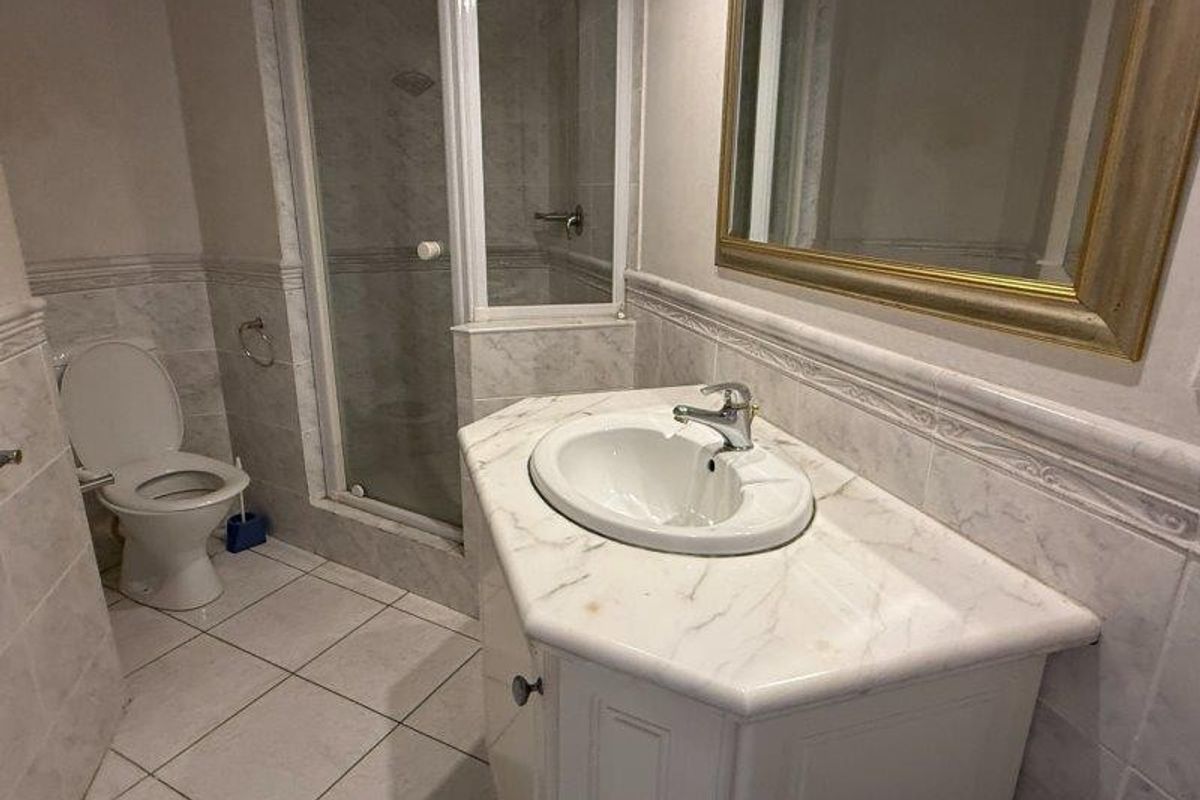 A functional bathroom featuring a marble-topped vanity, a separate shower enclosure with glass doors, and tiled walls and flooring.