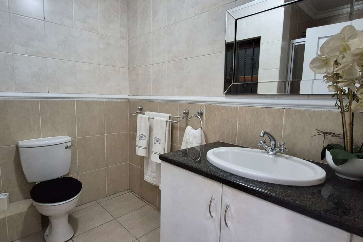 A functional bathroom featuring a vanity with a granite countertop, ceramic basin, wall-mounted mirror, and a standard toilet with tiled walls and flooring.