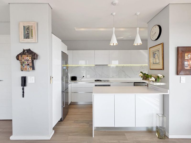 Modern kitchen featuring sleek white cabinetry, stone countertops, a marble-look splashback, integrated appliances, and a functional island with pendant lighting.