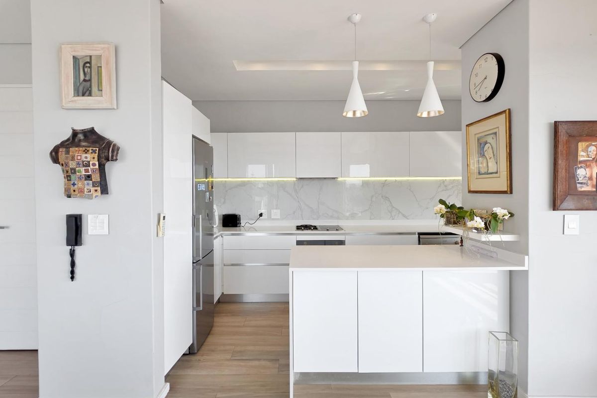 Modern kitchen featuring sleek white cabinetry, stone countertops, a marble-look splashback, integrated appliances, and a functional island with pendant lighting.