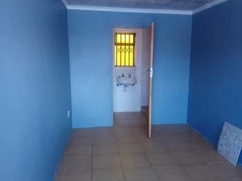 An empty bedroom featuring tiled flooring and a ceiling with tiles, leading to an adjacent small wash area with a wall-mounted basin.