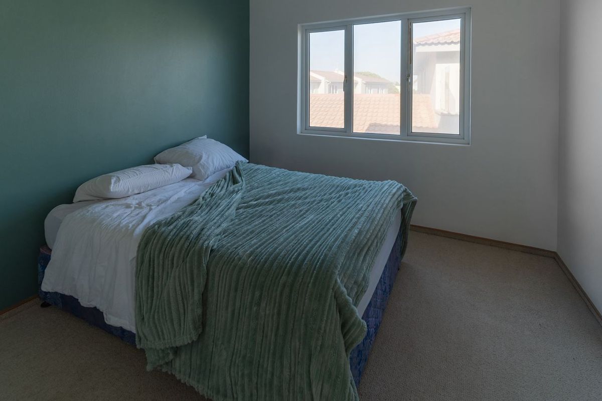 A bedroom featuring neutral carpeting and a green accent wall, with a large window providing natural light and views of the surrounding neighborhood.