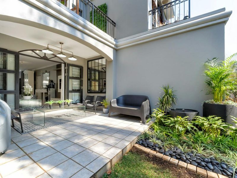 A well-maintained covered patio featuring tiled flooring, wrought iron railings, and seamless access to the interior living space through large glass doors.