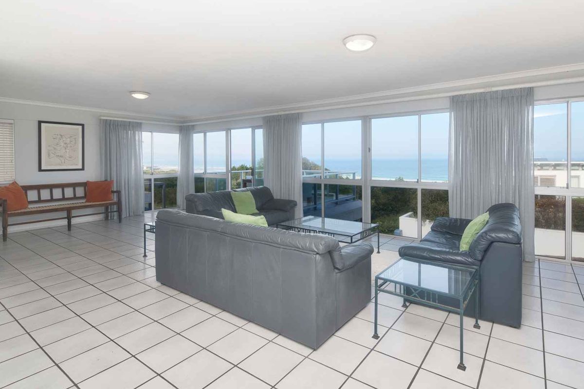 Spacious living room featuring large windows with panoramic ocean views and neutral tiled flooring throughout.