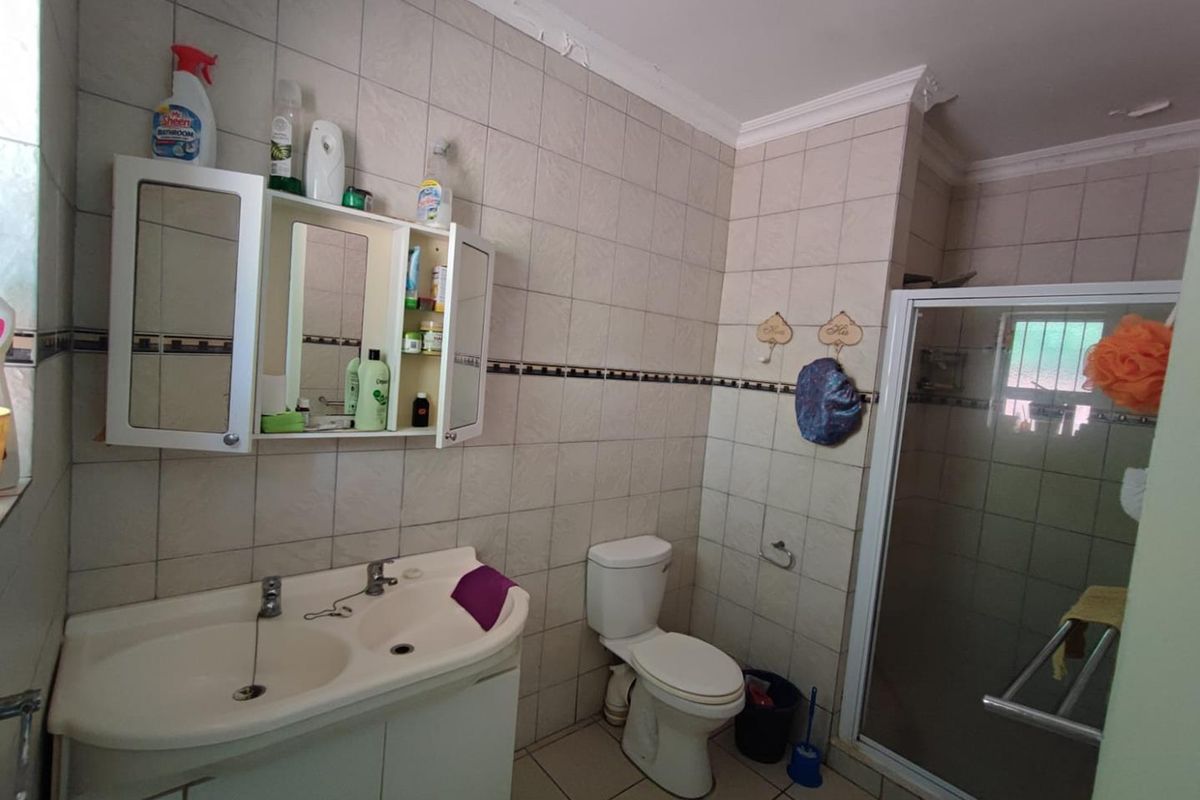 A functional bathroom featuring a double vanity with built-in cabinetry, a toilet, and a glass-enclosed shower with tiled walls.