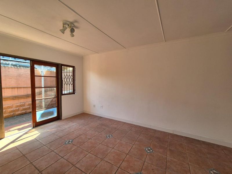 An empty living room featuring tiled flooring and a sliding glass door providing access to the exterior area.