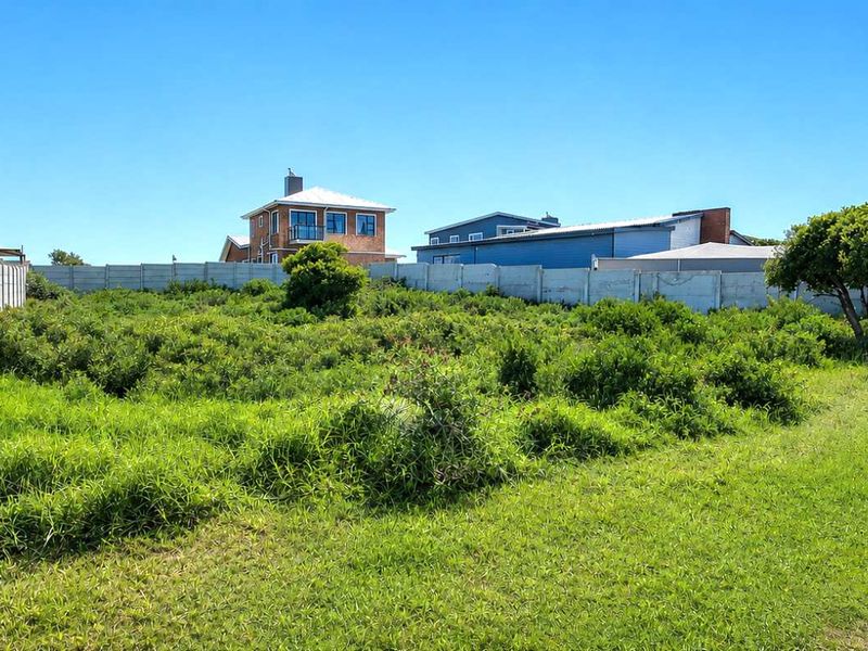 A vacant residential plot featuring a precast concrete boundary wall and direct access to an asphalt road in a developed neighborhood.