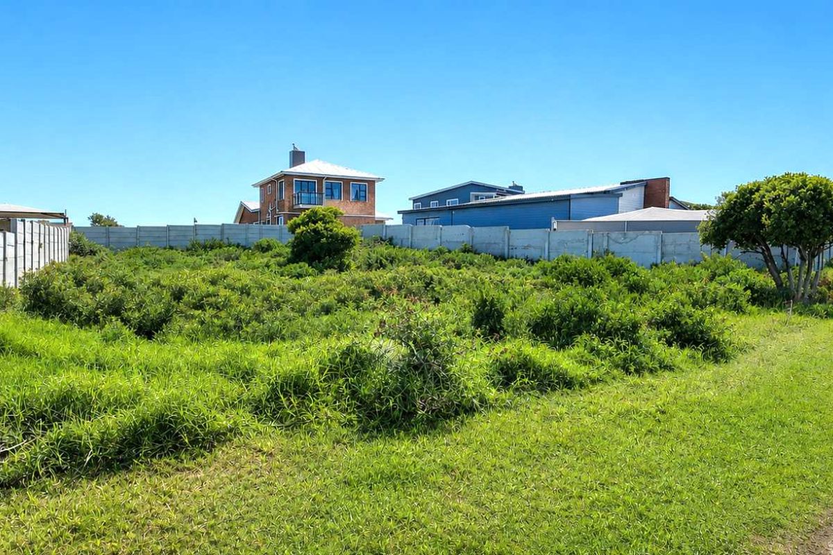 A vacant residential plot featuring a precast concrete boundary wall and direct access to an asphalt road in a developed neighborhood.