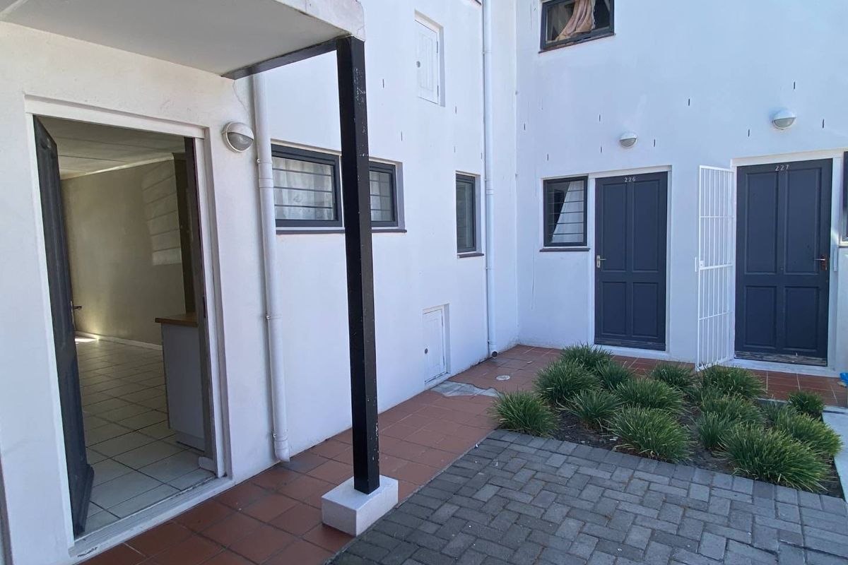 Exterior view of an apartment complex courtyard featuring paved walkways, landscaped garden beds, and access doors to individual units.