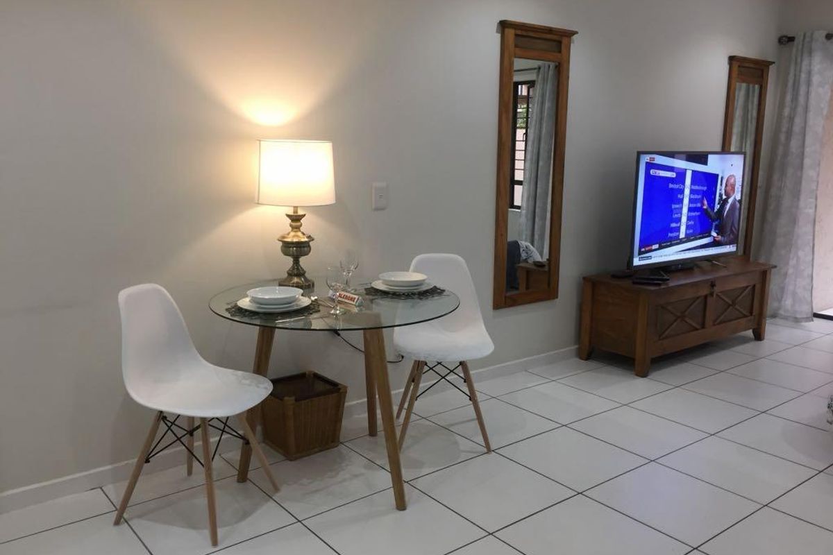 A bright living area featuring neutral tiled flooring and wall-mounted wooden mirrors, providing a clean and functional space for relaxation and dining.