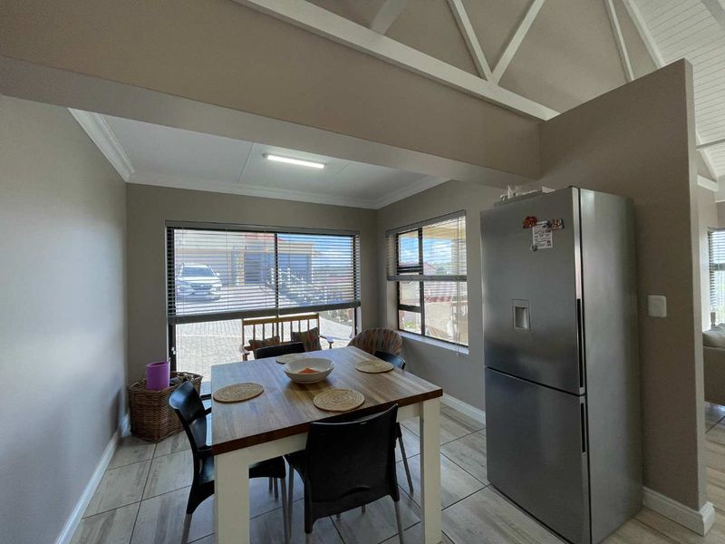 Open plan dining area featuring tiled flooring, exposed roof trusses, and large windows with venetian blinds, creating a bright and functional living space.