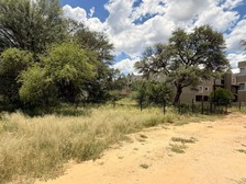 A vacant residential plot featuring natural vegetation, mature trees, perimeter fencing, and an existing carport structure.