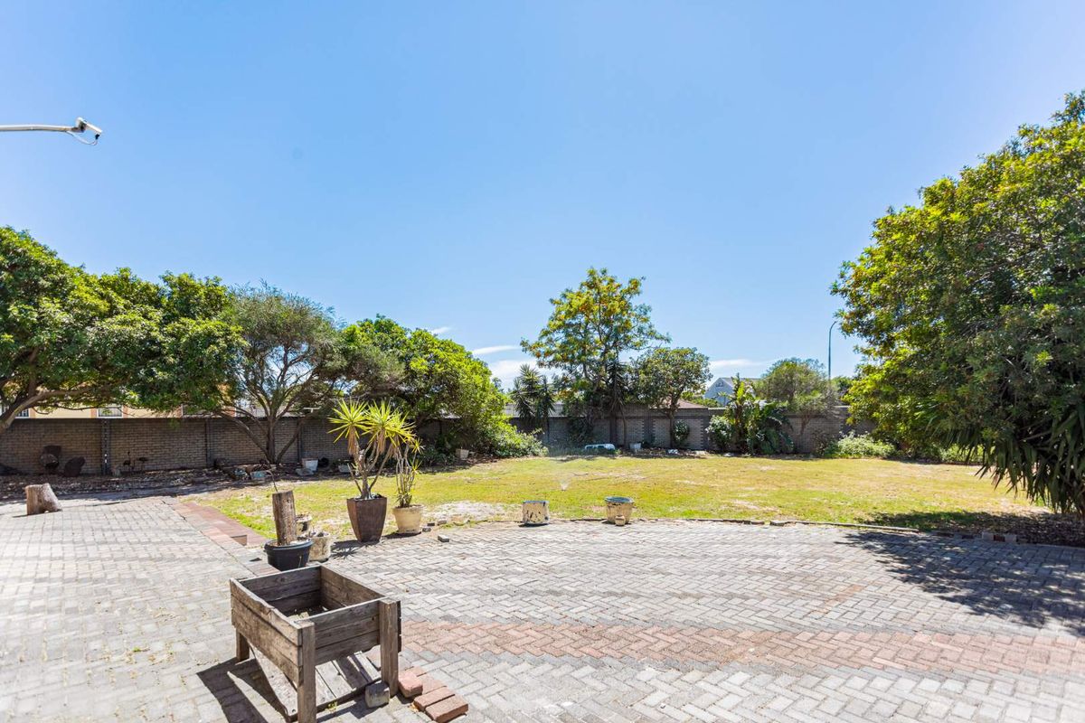 A spacious rear garden featuring a large brick-paved patio area and an expansive lawn enclosed by perimeter brick walls.