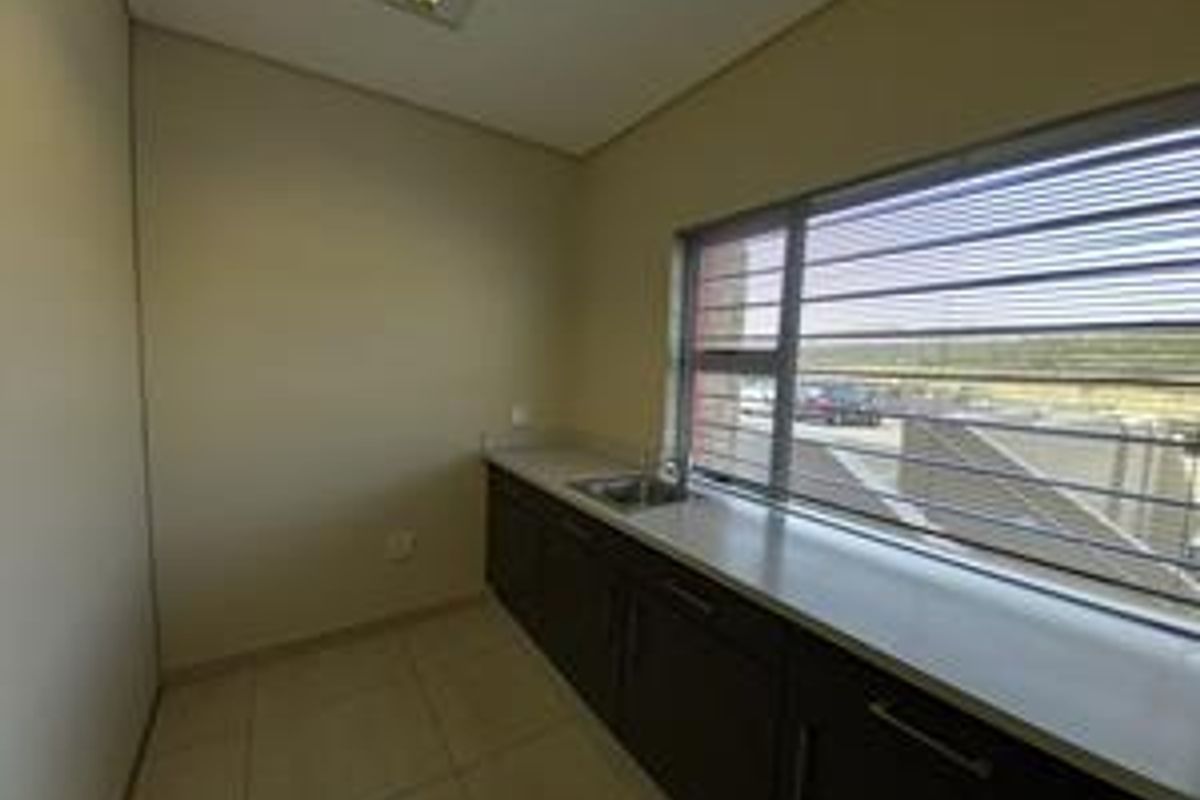 A functional kitchenette area featuring built-in dark cabinetry, a stainless steel sink, and large windows with security bars.