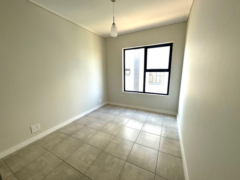 A clean, empty bedroom featuring neutral tiled flooring, a modern black-framed window, and a simple pendant light fixture.