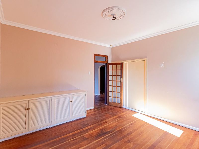 A spacious bedroom featuring original timber flooring, built-in cabinetry, a classic ceiling rose, and a timber-framed glass door leading to the hallway.
