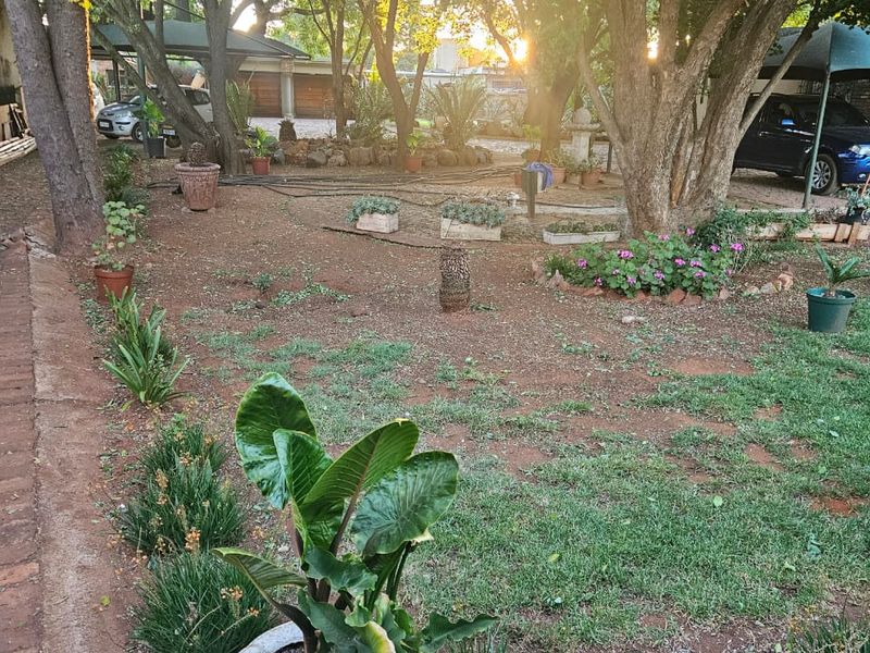 A spacious garden area featuring mature trees, established landscaping, and a brick-edged pathway, providing a natural outdoor setting for the cottage property.