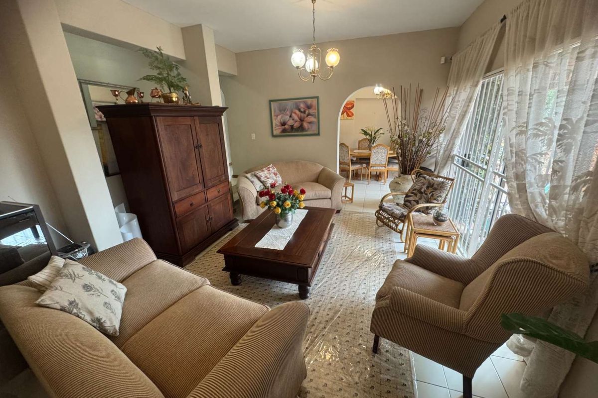 A spacious living room featuring tiled flooring, an arched entryway leading to the dining area, and large sliding glass doors with security gates.