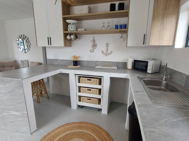 A modern kitchen featuring built-in cabinetry, stone-look countertops, open shelving, and a stainless steel sink with a mixer tap.