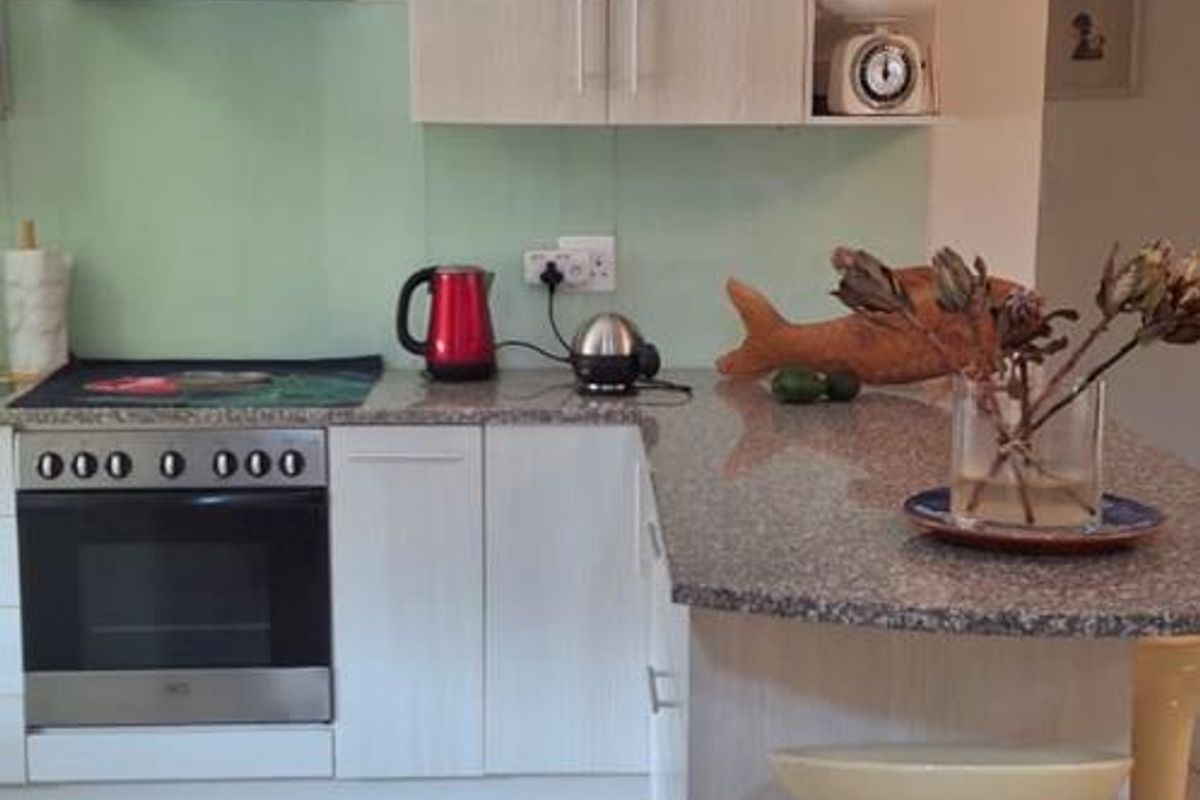 A functional kitchen featuring light wood-grain cabinetry, granite countertops, a glass splashback, and integrated stainless steel appliances including an oven and extractor fan.