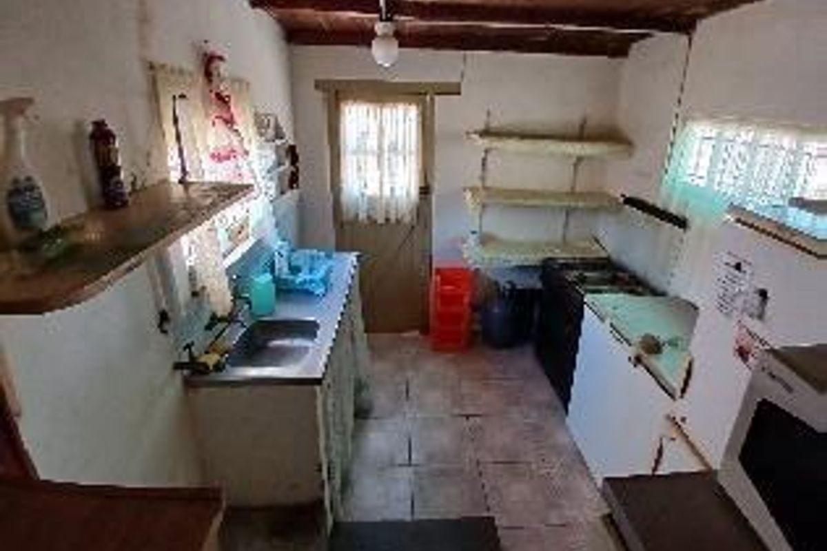 A functional, dated kitchen area featuring basic cabinetry, a stainless steel sink, and exposed timber ceiling beams.