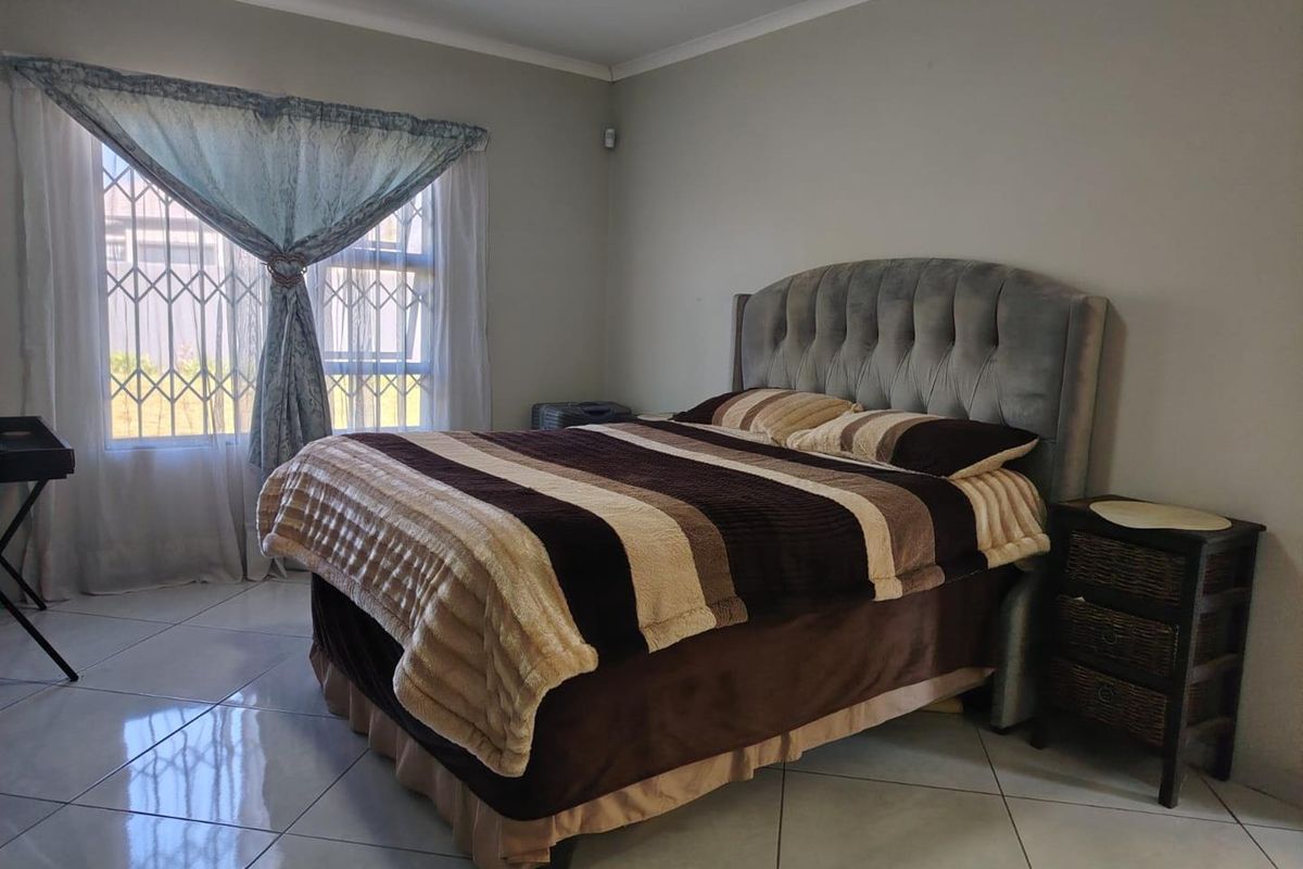 A well-lit bedroom featuring tiled flooring, a large window with security bars, and neutral wall finishes.