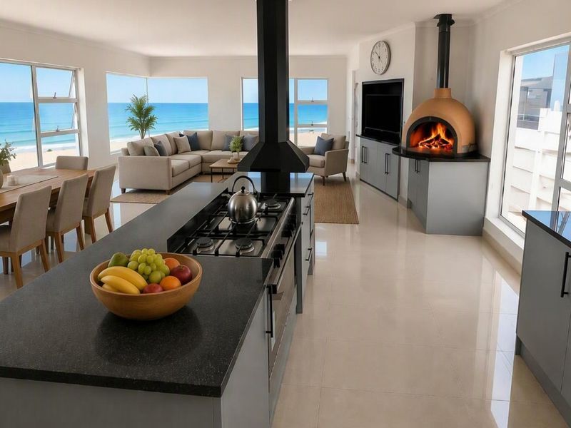 Spacious open-plan living area featuring a modern kitchen with island, built-in pizza oven, and expansive ocean views through large windows.