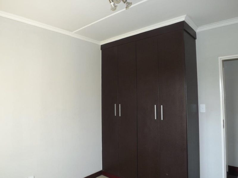 A clean, empty bedroom featuring dark wood-finish built-in cupboards, neutral wall paint, and ceiling cornice detailing.