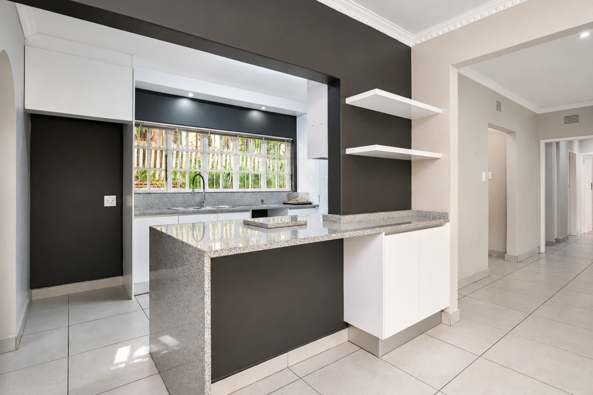 Modern kitchen featuring granite countertops, sleek cabinetry, floating shelves, and neutral ceramic floor tiles, offering a clean and functional culinary space.