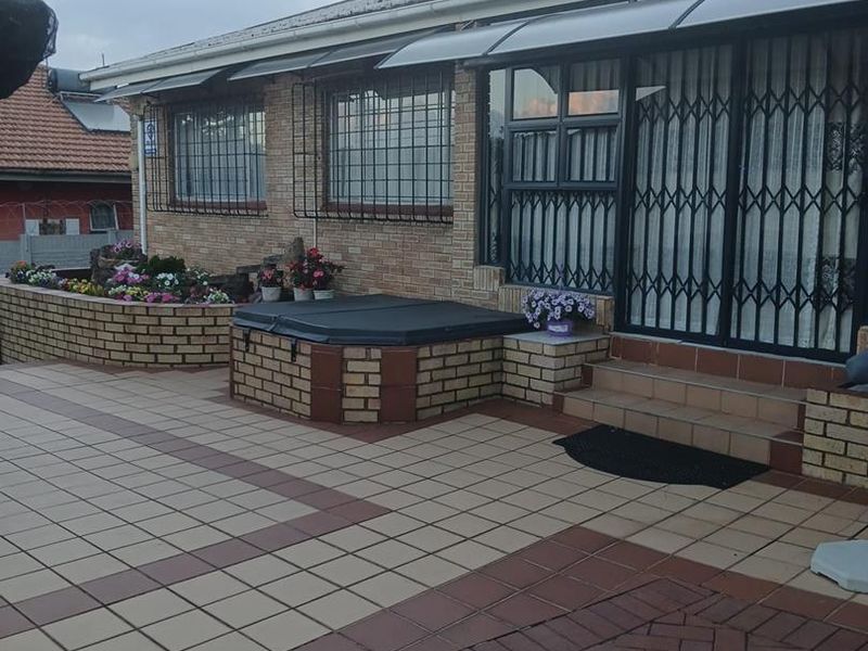 Rear exterior view featuring a paved patio, brick planter boxes, a built-in brick hot tub enclosure, and security gates over the sliding doors.