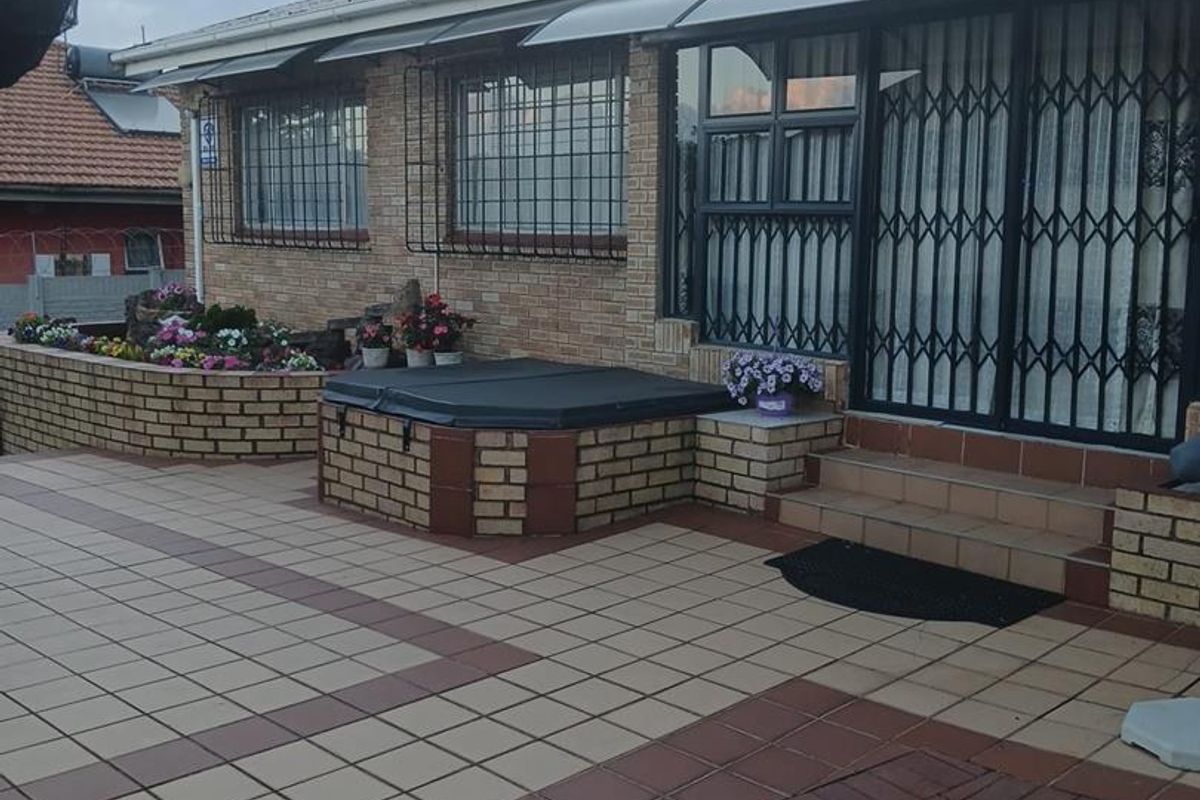 Rear exterior view featuring a paved patio, brick planter boxes, a built-in brick hot tub enclosure, and security gates over the sliding doors.