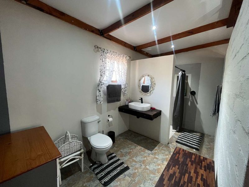 A rustic-style bathroom featuring exposed timber ceiling beams, a vessel sink on a floating vanity shelf, and a separate shower area.