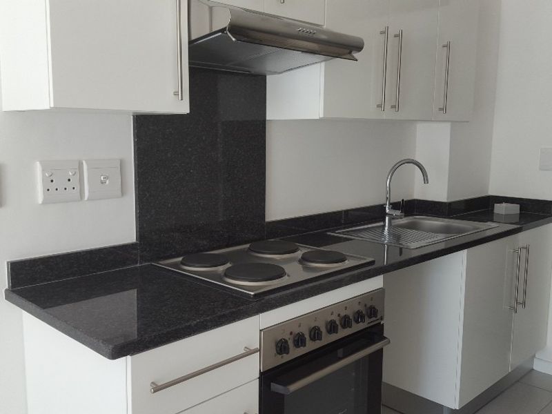 Modern kitchen featuring white cabinetry, granite countertops, a built-in oven, electric hob, and stainless steel sink.