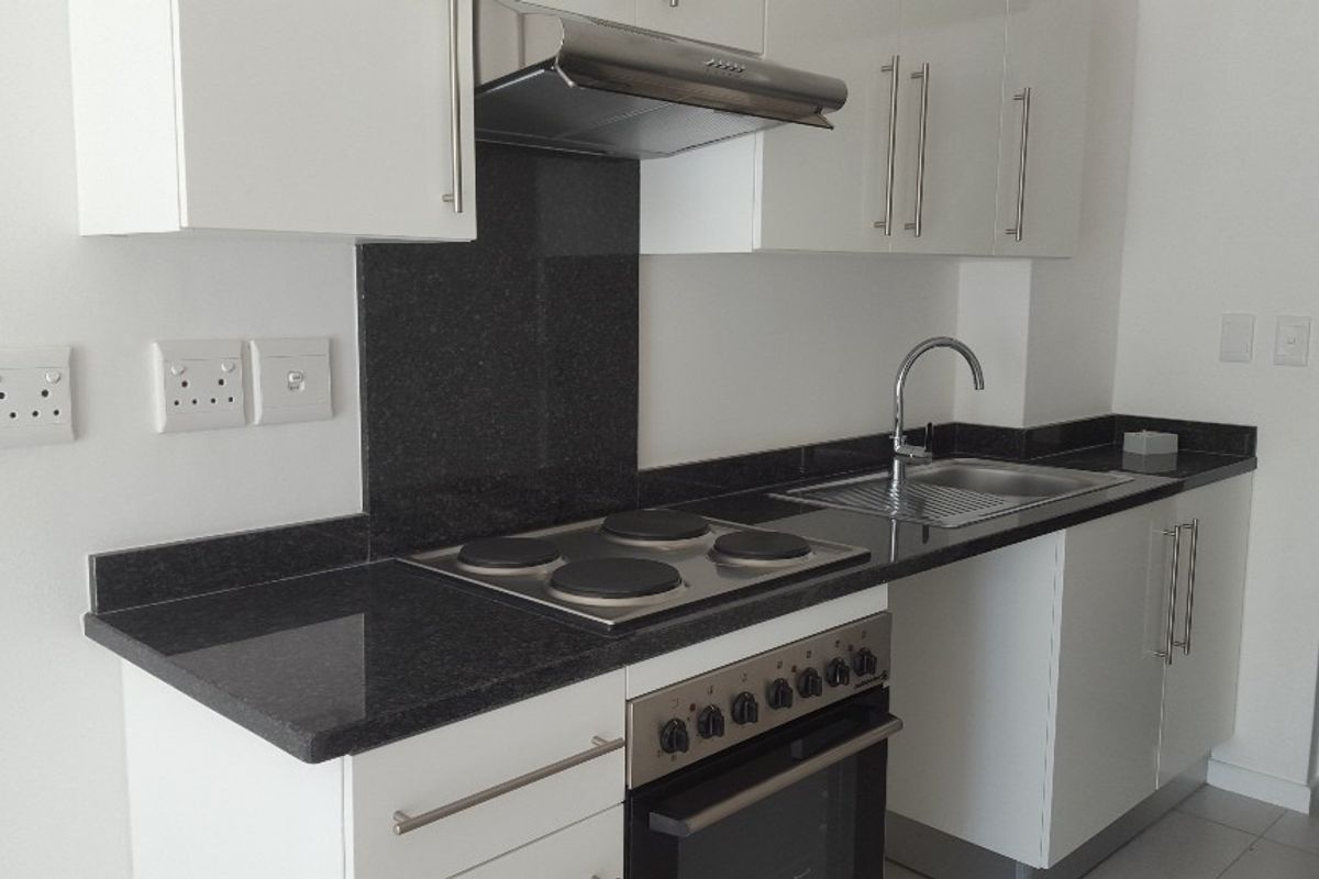 Modern kitchen featuring white cabinetry, granite countertops, a built-in oven, electric hob, and stainless steel sink.