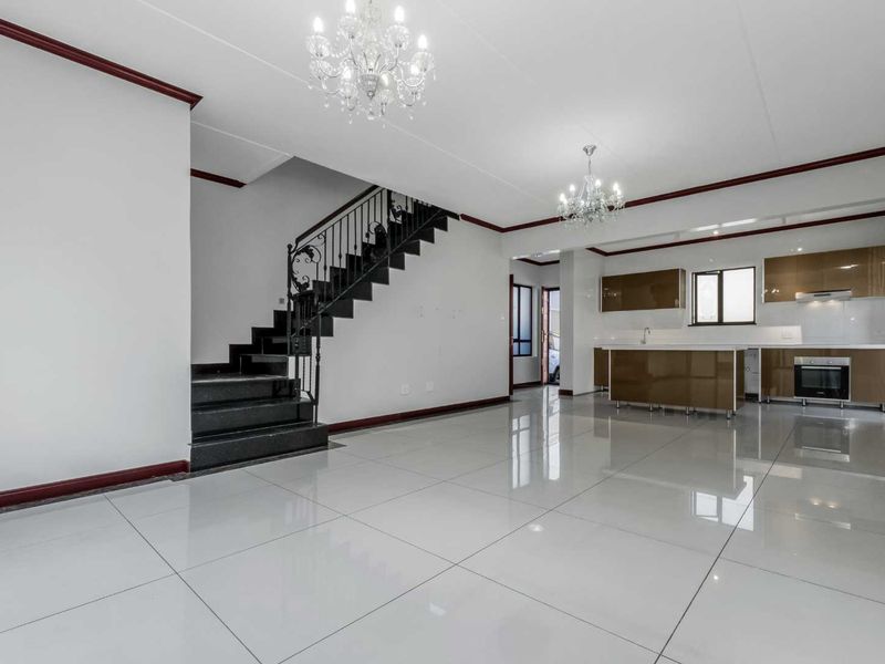 Spacious open-plan living area featuring polished porcelain tiles, a modern kitchen with built-in appliances, and a striking staircase with wrought iron detailing.