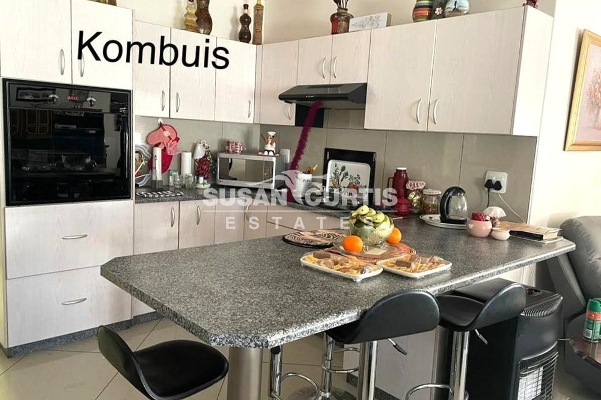 A functional kitchen featuring light-toned cabinetry, granite countertops, a breakfast bar, and integrated appliances including an oven and extractor fan.