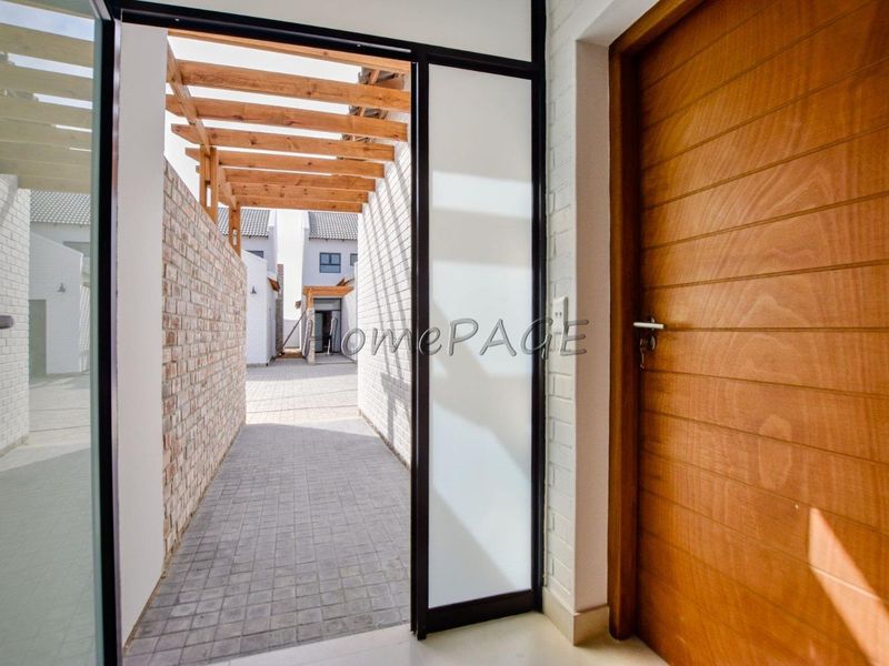 Entrance area featuring a timber front door, a modern glass door, and a paved walkway leading to an outdoor timber pergola.