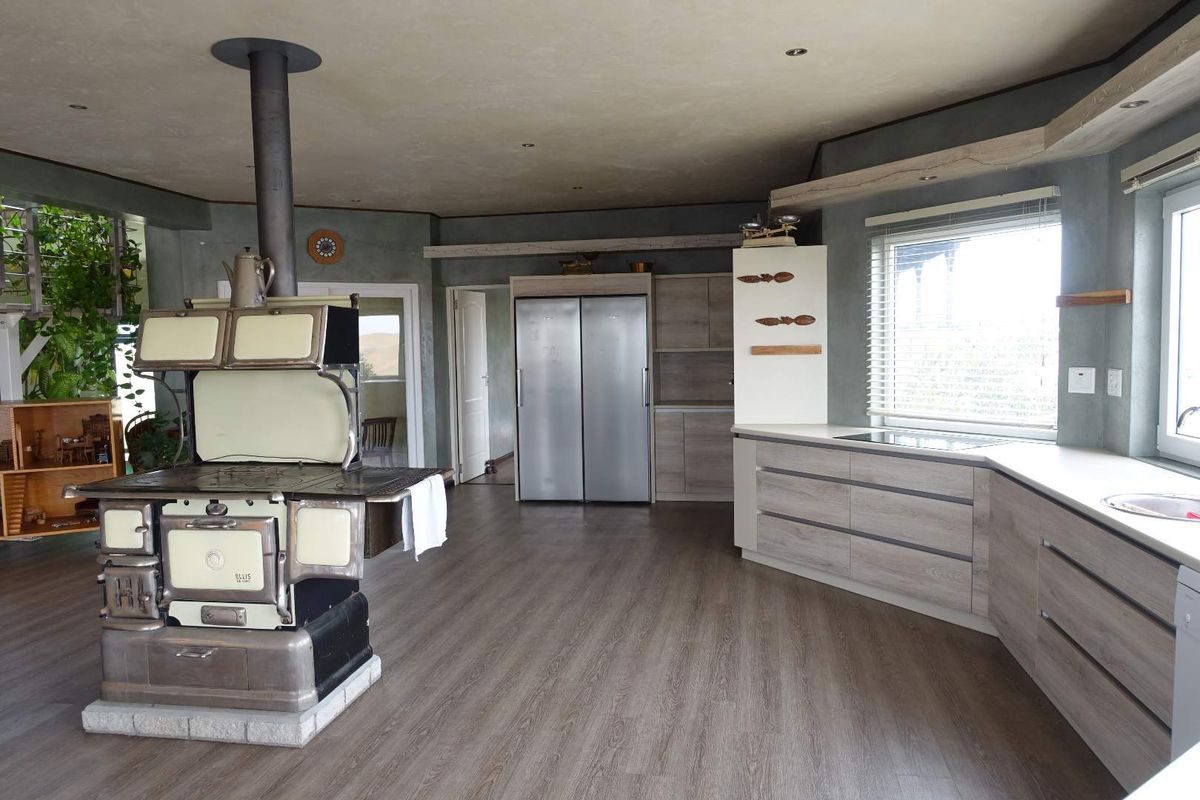 Spacious kitchen featuring modern cabinetry, integrated appliances, and a prominent vintage-style wood-burning stove with a flue.