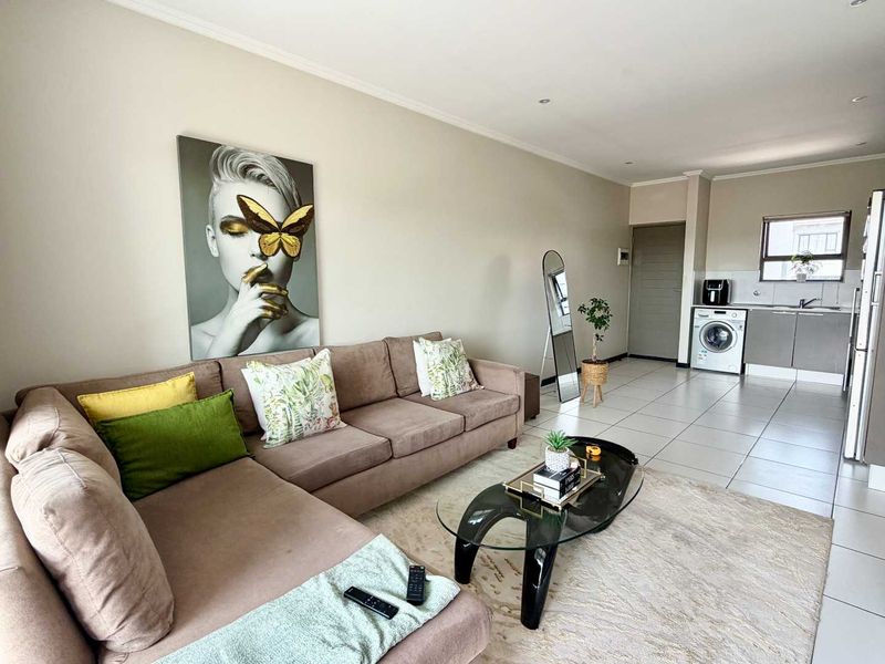 An open-plan living area featuring tiled floors, recessed lighting, and a compact kitchen corner with built-in cabinetry and laundry plumbing.