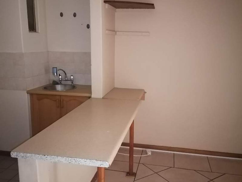 A compact kitchen area featuring built-in cabinetry, a sink, and a breakfast bar, requiring cosmetic updates to improve its overall condition.