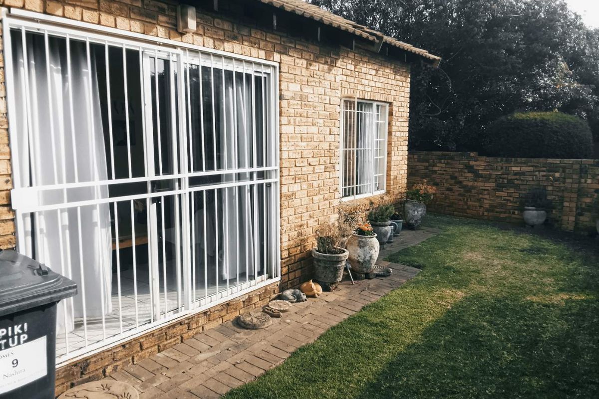 Rear exterior view of the townhouse featuring a face brick facade, sliding glass door with security gate, and a private garden area.