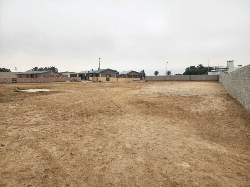 A vacant residential plot featuring a level sandy surface, enclosed by a perimeter wall, ready for development.