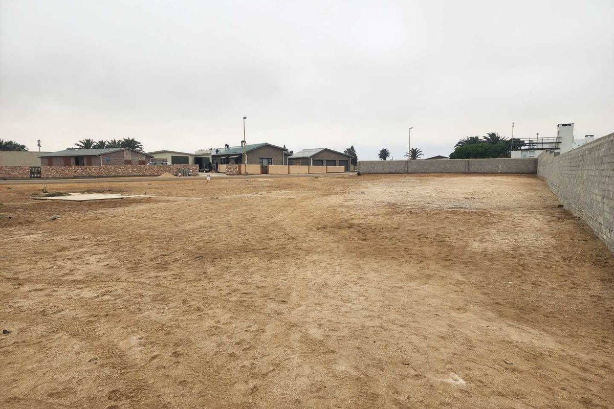 A vacant residential plot featuring a level sandy surface, enclosed by a perimeter wall, ready for development.