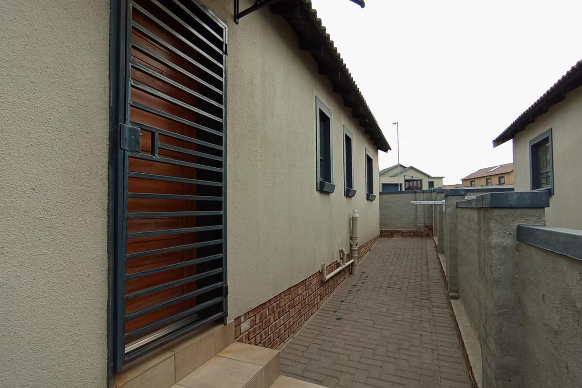 A side exterior view of the property featuring brick paving, a security gate, and boundary walls.