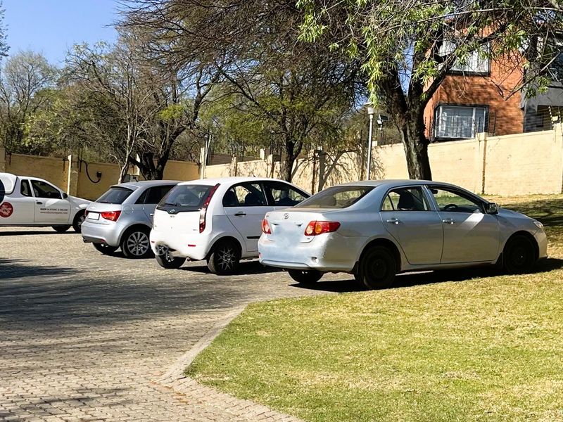 A paved driveway area with perimeter walling and established trees, serving as the front exterior approach to the townhouse property.